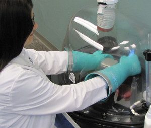 Female tech in lab coat works in clear dome glove box
