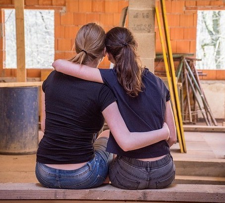 Friends embrace, 2 young women hold each other in construction space