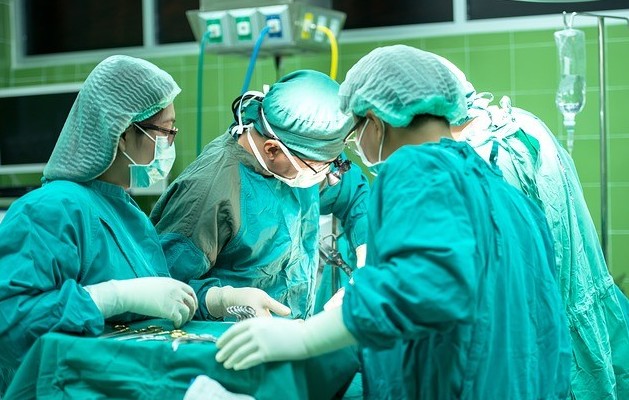 Surgical staff of four in blue-green gowns operate on a patient